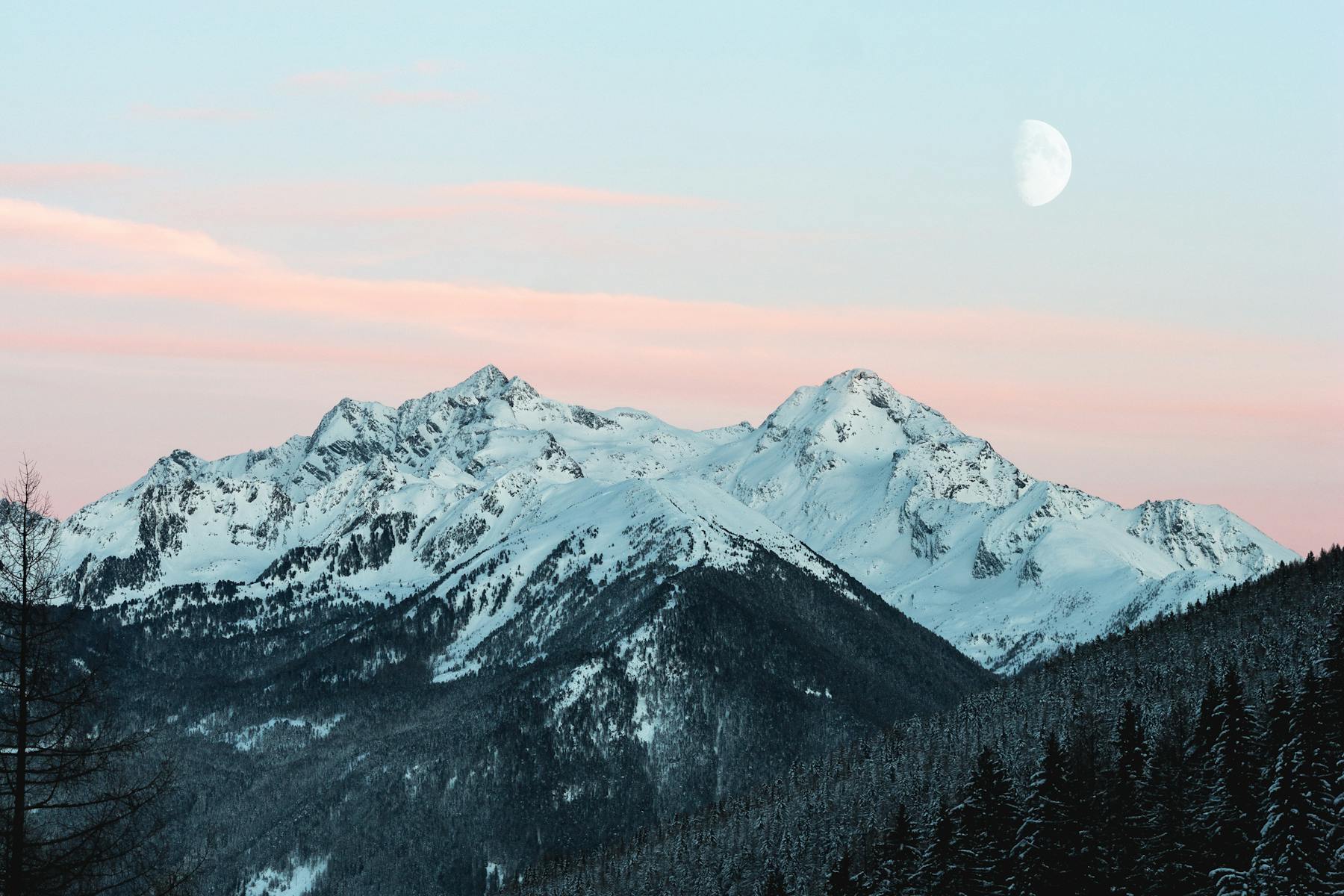 Snow-capped mountain peaks at dusk beneath a rising moon